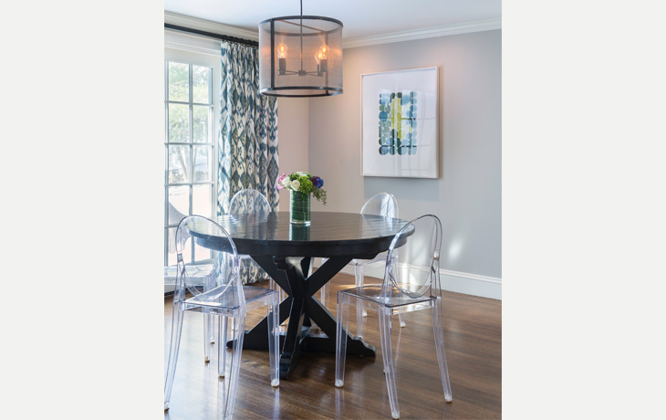 Dark table contrasts iconic “Ghost” chairs and contemporary artwork in a casual dining area by Blue Jay Design of Wellesley, MA