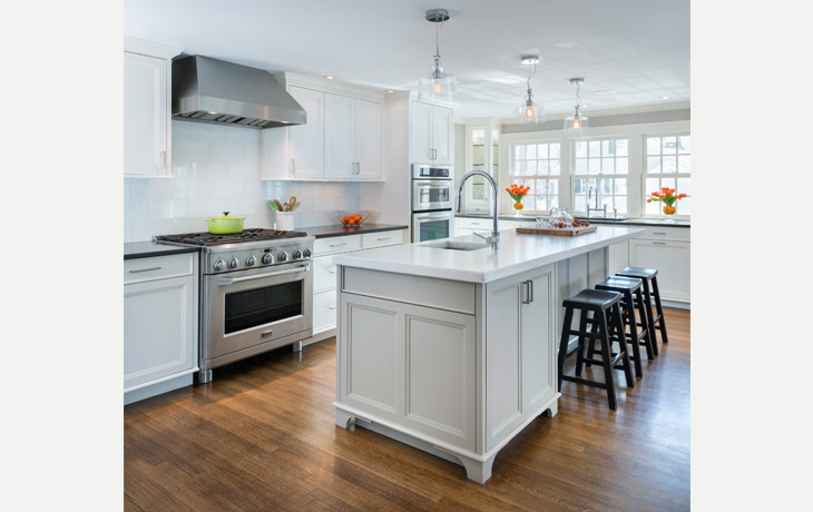 Modern, oversized glass tiles and clear glass pendants harmonize with traditional cabinetry in a kitchen by Blue Jay Design of Wellesley, MA